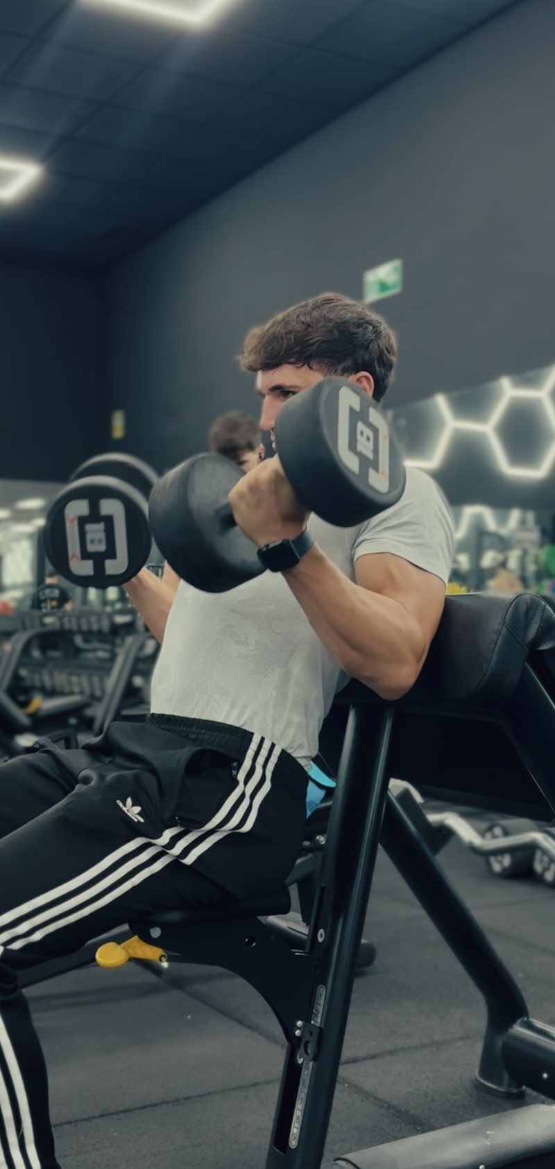 Aaron haciendo curl de bíceps con mancuernas en el banco predicador